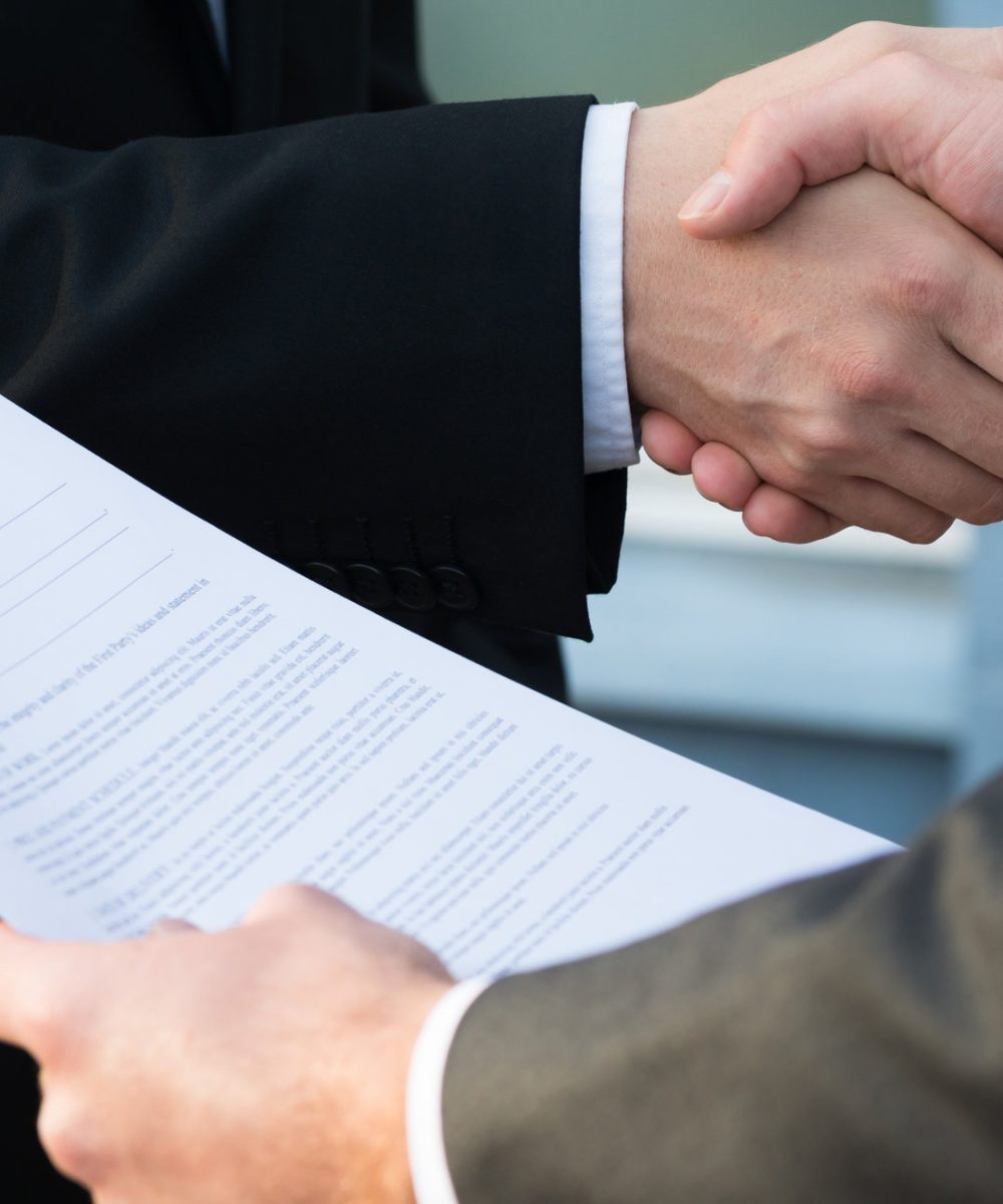 Cropped image of businessman shaking hands with partner while holding contract papers